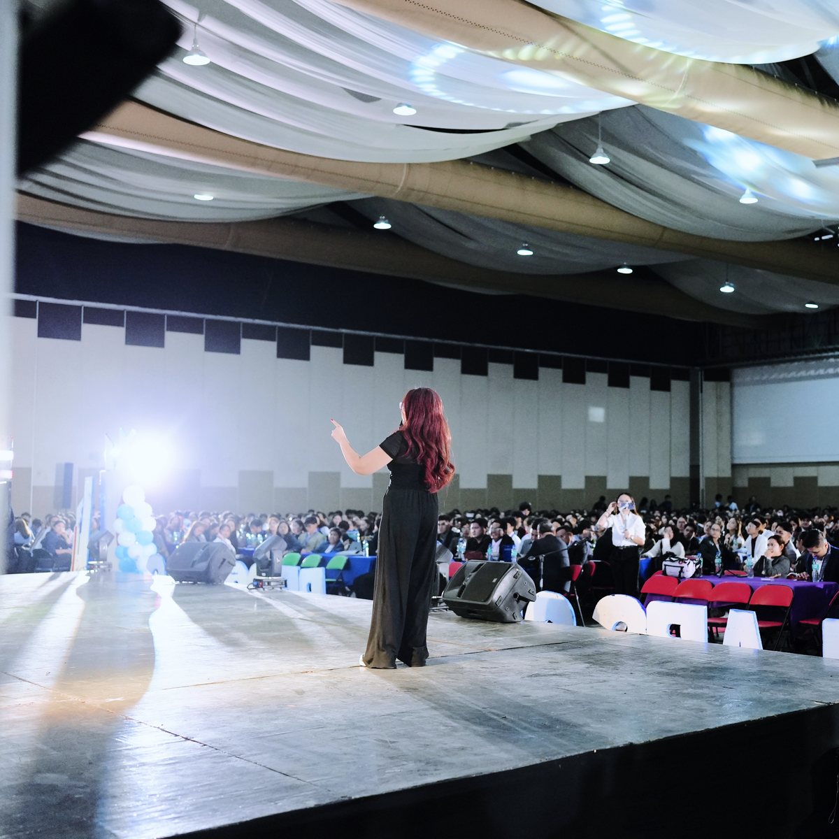 Nikki speaking on a big stage to a packed conference hall